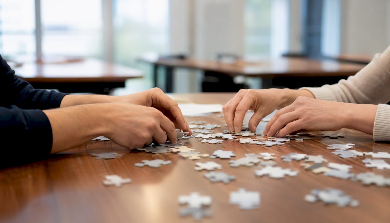 Zwei Hände, die Puzzleteile zu einem Ganzen zusammensetzen – ein Bild, das perfekt für die Verbindung von Präsenz- und Online-Lernen steht.